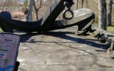 Puhelimen näyttö, jonka takana näkyy vanha ankkuri.