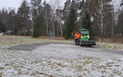 Pellolla frisbeegolfkori ja mies traktorin kanssa taustalla metsää