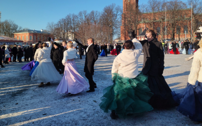 Nuoria tanssii näyttävissä juhlamekoissa, takeissa ja frakeissa ulkona aurinkoisessa ja hieman lumisessa säässä.