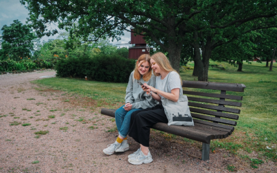 Kaksi tyttöä istuu puistonpenkillä ja katsovat puhelinta.