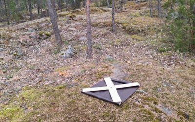 Valkoinen X-mallinen signaalimerkki alkukevään harmahtavassa maastossa.