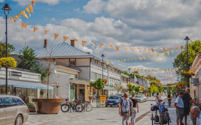 Kuva Aliseltakadulta, kuvassa ihmisiä kävelemässä kadulla. Kesäiset juhlaviirinauhat on ripustettu katuvalaisimiin.