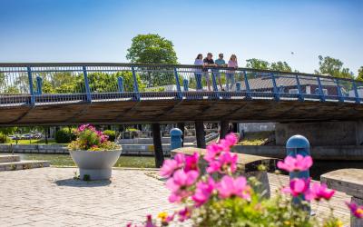 Ihmisiä Sorvakon sillalla katsomassa merelle. Etualalla kesäkukkia.