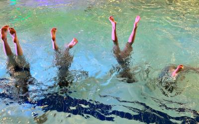 4 tyttöä seisoo käsillä uima-altaassa, varpaat pinnalla