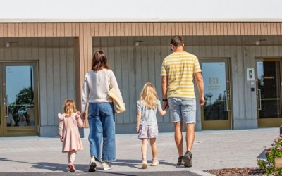 Kaksi lasta ja kaksi aikuista kävelee käsi kädessä kohti päiväkotia.