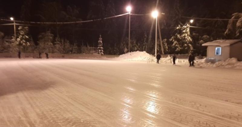 iltakuva luistelukentästä, muutama luistelija ja valot kentän yllä