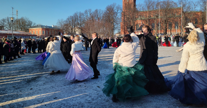 Nuoria tanssii näyttävissä juhlamekoissa, takeissa ja frakeissa ulkona aurinkoisessa ja hieman lumisessa säässä.