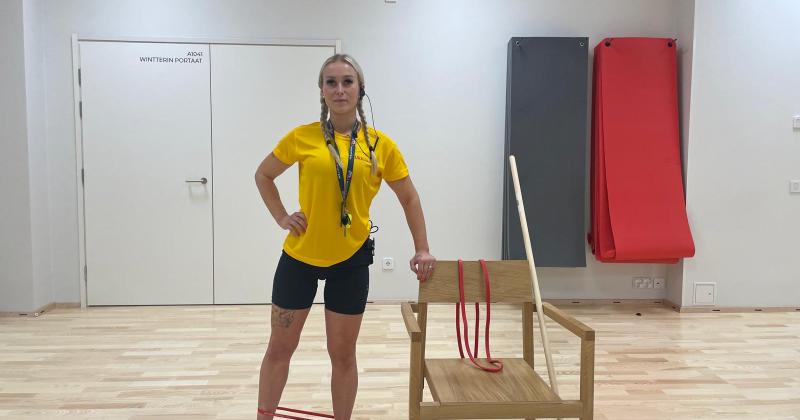 nainen ohjaa tasapainojumppa seisten, vierellä tuoli