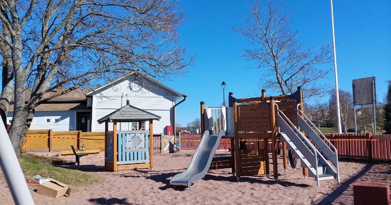 Pakkahuoneen leikkikenttä keväisen aurinkoisessa säässä. Kuvassa näkyy leikkiväline, jossa on liukumäki ja pieni leikkikatos.