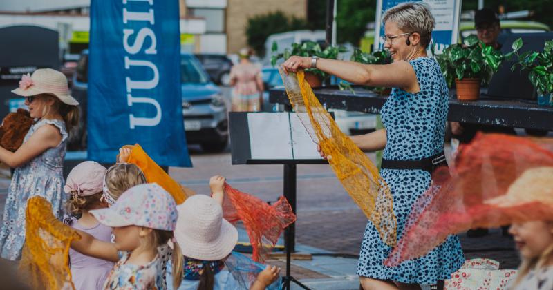 Lapset tanssivat torilla värikkäiden huivien kanssa.