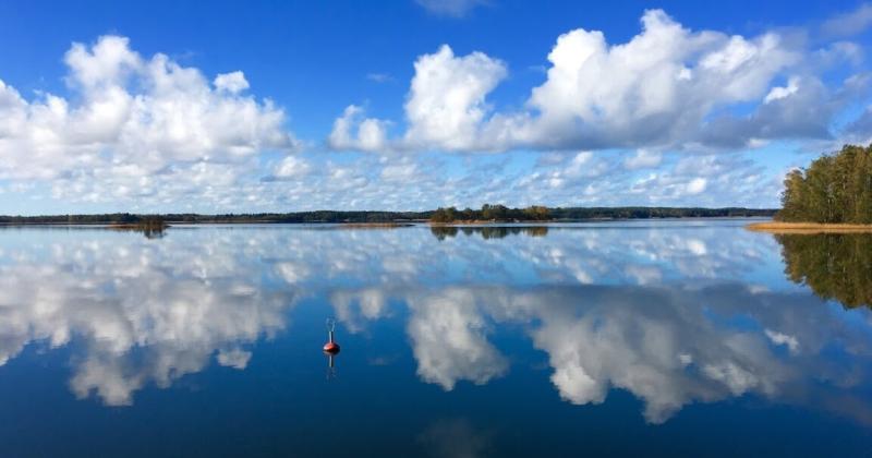 Merimaisema, pilvet heijastuvat tyynestä veden pinnasta.