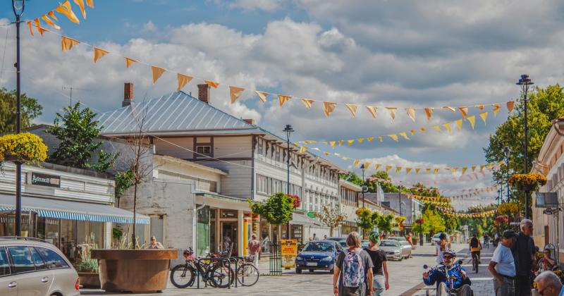 Kuva Aliseltakadulta, kuvassa ihmisiä kävelemässä kadulla. Kesäiset juhlaviirinauhat on ripustettu katuvalaisimiin.