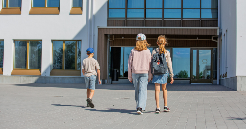 Kaksi tyttöä ja yksi poika kävelee kohti Wintterin koulurakennuksen sisäänkäyntiä. 