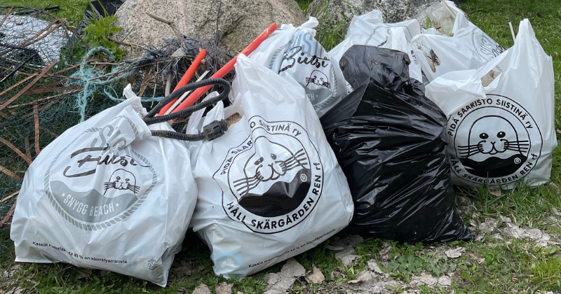 Kuvassa täyteen kerättyjä roskapusseja luonnossa. Roskapusseissa lukee "Pidä saaristo siistinä"