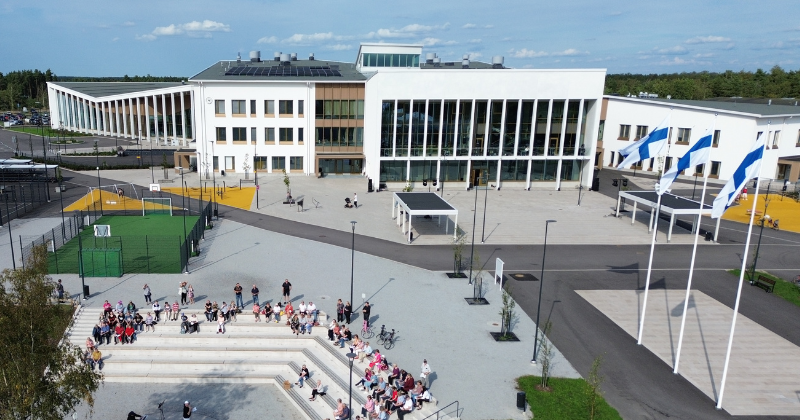 Ilmakuva monitoimijatalo Wintteristä kesäisenä päivänä. Rakennuksen edustalla liehuu Suomen liput ja ulkoportailla istuu ihmisiä.