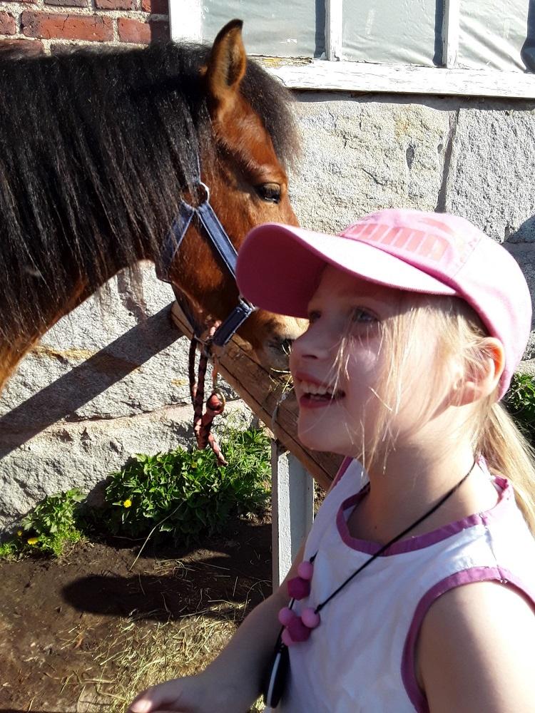 Lapsi ja hevonen tallin ulkopuolella.